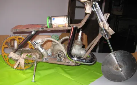 Kreatives Motorrad aus Altmetall, mit einem 50-Euro-Geldschein im Glas als Tank und einem kleinen Motorradhelm-Anhänger.