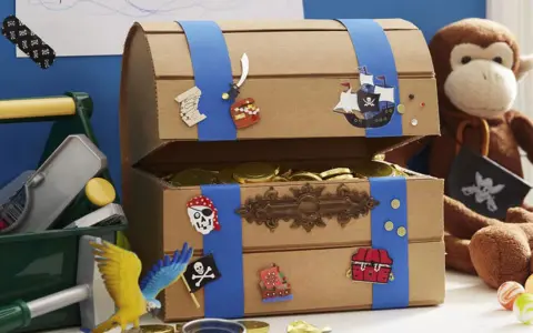 Bastelidee: Eine Schatztruhe aus Pappe, verziert mit Piratenmotiven und gefüllt mit Goldmünzen. Ein Affe hält eine Piratenflagge.