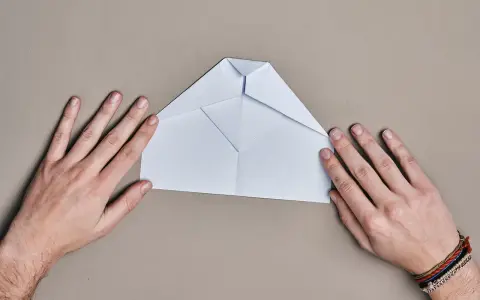 Hände falten einen weißen Papierflieger. Der runder Papierflieger nimmt langsam Form an.