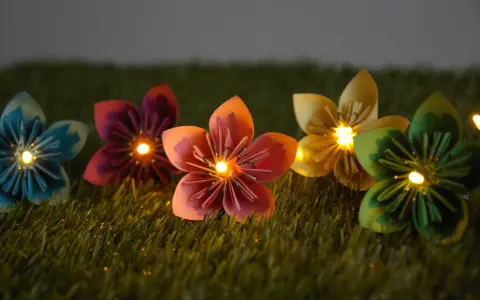 Bunte Papierblumen leuchten auf grünem Gras. Eine selbstgebastelte Lichterkette, die Kinder lieben werden.