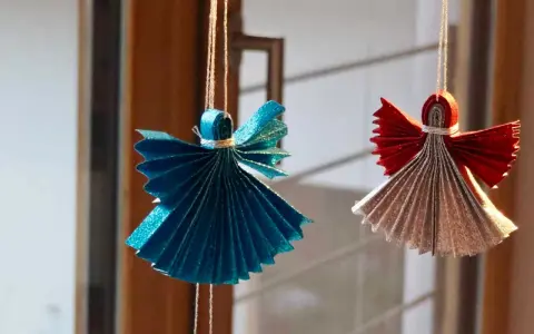 Zwei glitzernde Origami Weihnachts Engel, einer in Blau, der andere in Rot und Silber, hängen an Fäden.