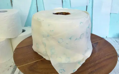 Eine Torte aus Toilettenpapier basteln: Ein realistisch aussehender Kuchen in Form einer Toilettenpapierrolle, verziert mit blauen Blumenmustern.