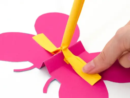 Hand bastelt fliegende Schmetterlinge aus pinkem Papier. Ein gelber Streifen wird befestigt.