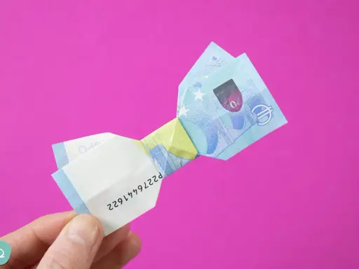 Ein 20-Euro-Schein ist zu einer Schleife gefaltet. Ein Finger hält das gefaltete Geld.