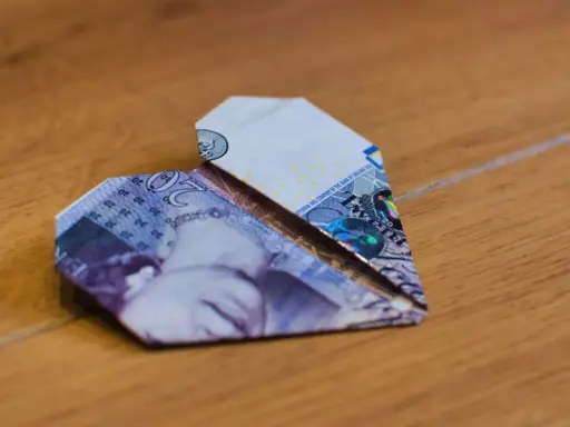 Ein Herz aus gefalteten Geldscheinen liegt auf Holz. Die Noten zeigen die Zahl 20.