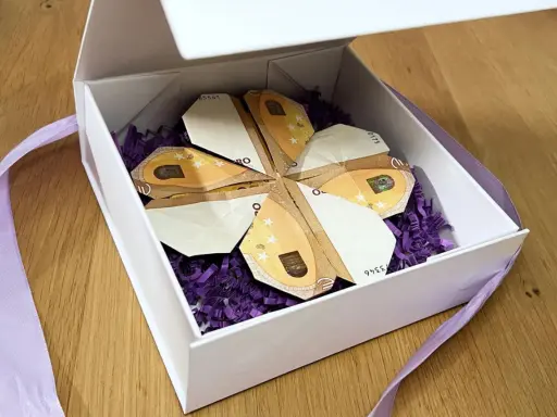 Ein Geschenk: Geld falten blatt in Form eines Kleeblatts, liebevoll in einer weißen Schachtel mit lila Füllung und Band arrangiert.