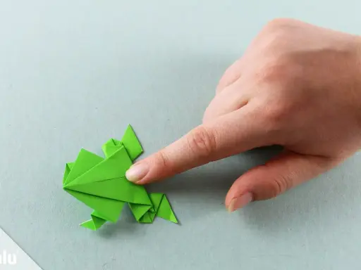 Grüner Origami-Frosch wird von einer Hand geformt. Eine einfache origami vorlage zum Nachfalten.