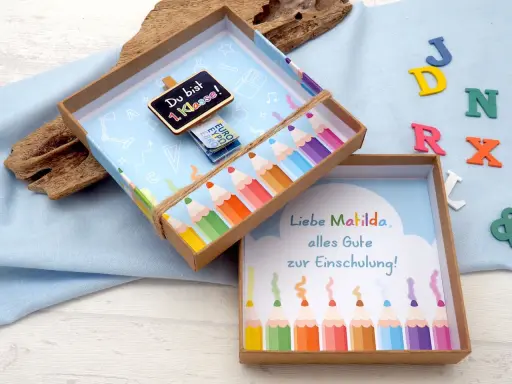Kreatives Geldgeschenk zur Einschulung basteln: Eine Schultüte mit Bleistiften und einer Tafel "Du bist 1. Klasse!".