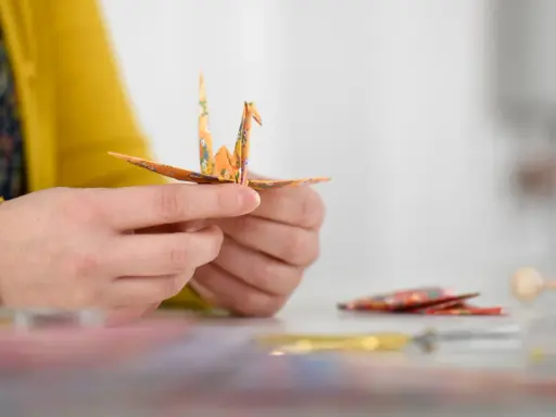 Hände falten einen Kranich aus buntem Papier. Ein schöner Moment während eines Origami Kurses.