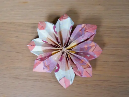 Eine kunstvolle Geld falten Tulpe aus Euro-Scheinen, die auf einer Holzoberfläche liegt.