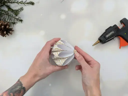 Hände basteln mit Klebepistole und Papier einen schönen DIY Christbaumschmuck. Tannenzweige und Orangenscheiben liegen bereit.