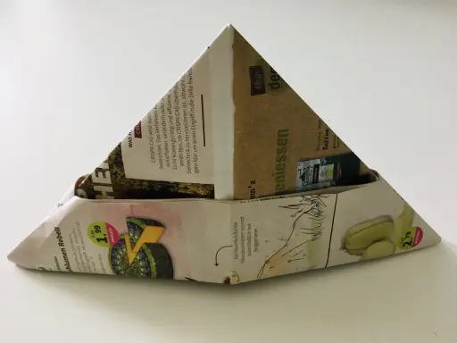 Ein dreieckiger Papierhut, gefaltet aus Zeitungspapier mit Werbung für Käse und Kaffee. Das Papierhut falten ist eine einfache Bastelidee.