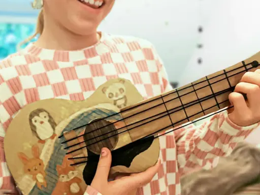 Kind bastelt Gitarre nach Vorlage. Die selbstgemachte Gitarre ist mit süßen Tieren wie Pinguin, Panda, Hase und Fuchs bemalt.