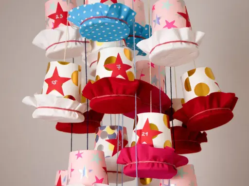 Bunte Becher mit Sternen und Punkten, die als Adventskalender becher basteln dienen. Jede Tasse hat eine Zahl und eine Stoffkappe.