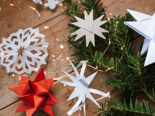 Zauberhafte Papier bastelideen Weihnachten einfach: Sterne aus Papier, Tannenzweige und Lichterkette auf Holz.