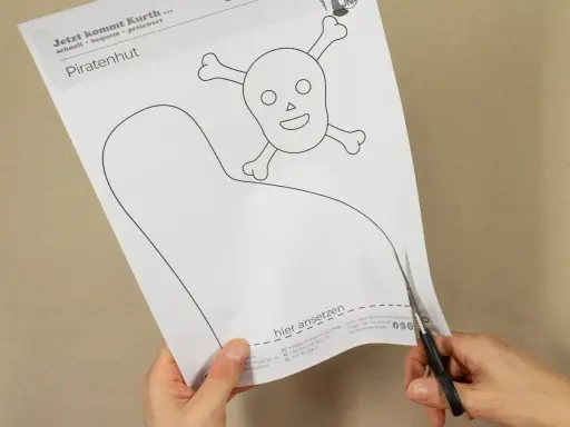 Schere schneidet Vorlage für einen Piratenhut mit Totenkopf. So einfach lässt sich ein Piratenhut basteln!