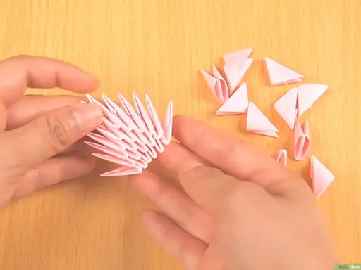 Hände bauen mit rosa Papierstücken ein 3D-Origami-Tier. Die Anleitung ist leicht verständlich.