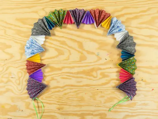 Bunte Papierfächer, die zu einer ziehharmonika-girlande gebastelt wurden, liegen auf einer Holzplatte.