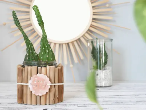 Zwei Kakteen in einem selbstgemachten Blumentopf aus Holzstäbchen. Ein Schild mit "STAY ALIVE" hängt daran.