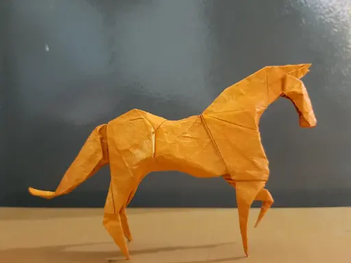 Ein orangefarbenes Origami-Pferd steht auf einem Tisch.