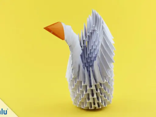 Ein weißer Schwan aus modularem Origami mit orangefarbenem Schnabel steht vor einem gelben Hintergrund.