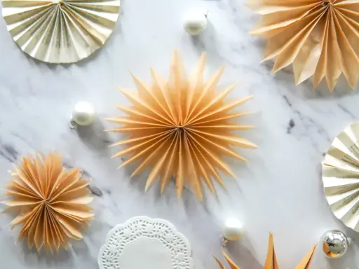 Fächersterne aus Papier, wie bei einer Teebeutel falten Anleitung, schmücken den Marmortisch neben Weihnachtskugeln.