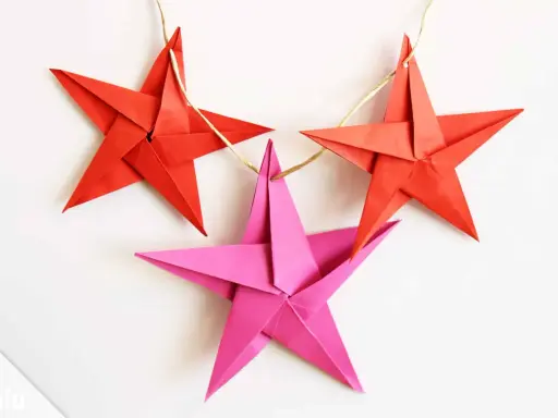 Drei bunte Sterne Origami hängen an einer Schnur. Rote Sterne und ein pinker Stern, perfekt für Weihnachtsdekoration.