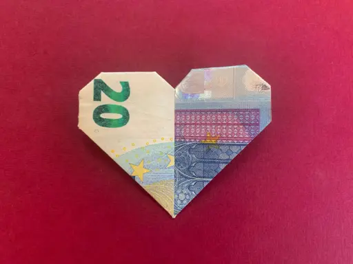 Ein gefaltetes Herz aus 20-Euro-Scheinen auf rotem Untergrund.