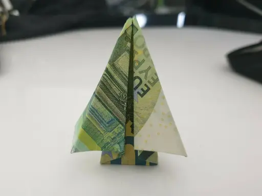 Ein kleiner, gefalteter Baum aus Geldscheinen steht auf einem Tisch. Ein kreativer geld falten baum.