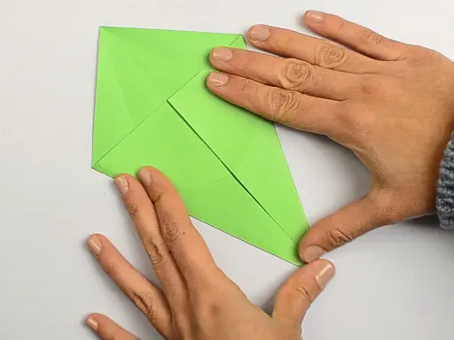 Hände falten ein grünes Papier, um einen einfachen Drachen zu basteln.