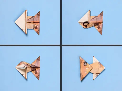 Vier gefaltete Geldscheine, die wie kleine Fische aussehen, schwimmen auf blauem Grund. Ein kreativer **fisch falten geld** Trick.