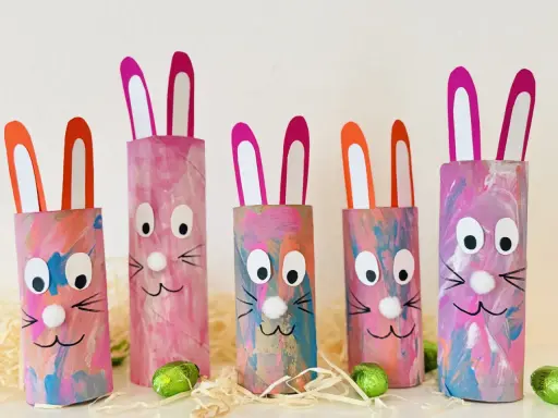 Fünf bunte Osterhasen aus Klopapierrollen mit großen Augen und rosa Ohren, dekoriert mit Pinselstrichen.