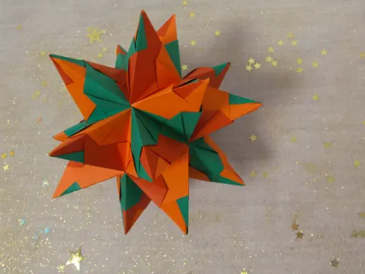 Ein sternförmiges Origami-Objekt in Orange und Grün, das an einen funkelnden Winterhimmel erinnert.
