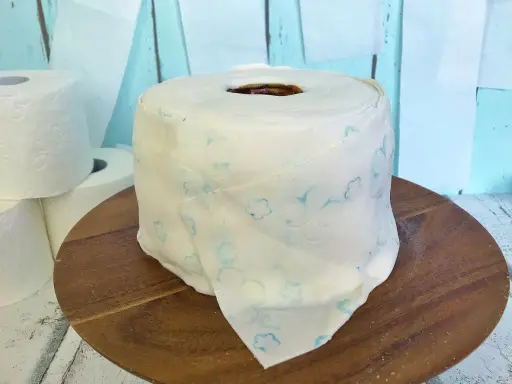 Eine Torte aus Toilettenpapier basteln: Ein realistisch aussehender Kuchen in Form einer Toilettenpapierrolle, verziert mit blauen Blumenmustern.