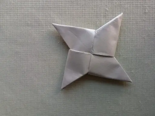 Ein silberner Papier-Wurfstern, perfekt zum **Wurfstern basteln**. Liegt auf einer texturierten, hellgrünen Unterlage.