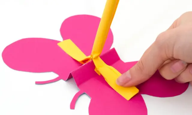 Hand bastelt fliegende Schmetterlinge aus pinkem Papier. Ein gelber Streifen wird befestigt.