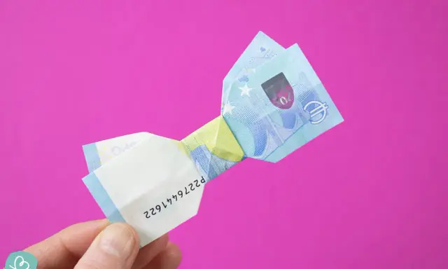 Ein 20-Euro-Schein ist zu einer Schleife gefaltet. Ein Finger hält das gefaltete Geld.