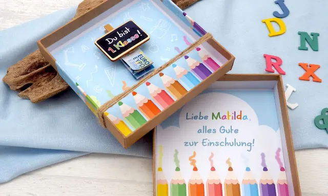 Kreatives Geldgeschenk zur Einschulung basteln: Eine Schultüte mit Bleistiften und einer Tafel "Du bist 1. Klasse!".