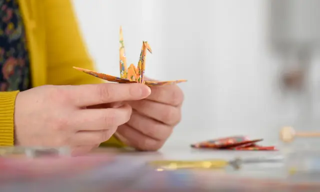 Hände falten einen Kranich aus buntem Papier. Ein schöner Moment während eines Origami Kurses.