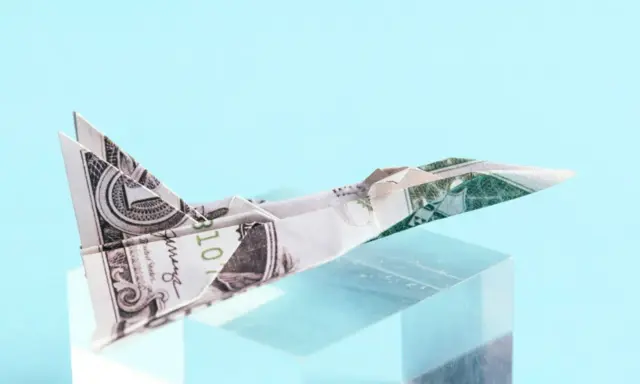 Ein **Flugzeug aus Geld falten** ist ein Kunstwerk. Ein Dollar-Schein wurde zu einem Jet gefaltet, der auf einem transparenten Block thront.