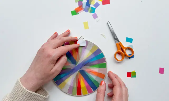 Hände basteln mit transparentsterne falten, bunte Streifen auf einem Kreis, daneben Schere und Konfetti.