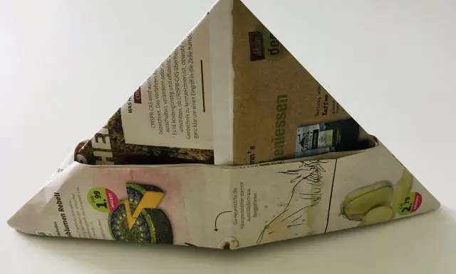 Ein dreieckiger Papierhut, gefaltet aus Zeitungspapier mit Werbung für Käse und Kaffee. Das Papierhut falten ist eine einfache Bastelidee.