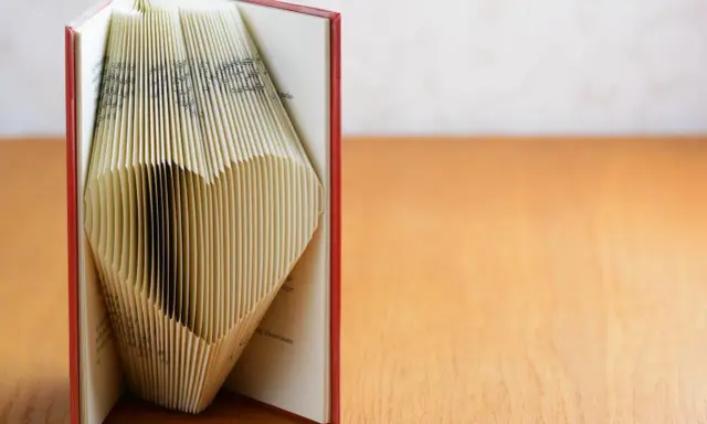 Ein Buch, dessen Seiten zu einem Herz gefaltet sind. Eine kreative Idee für ein Geldgeschenk, Buch basteln.