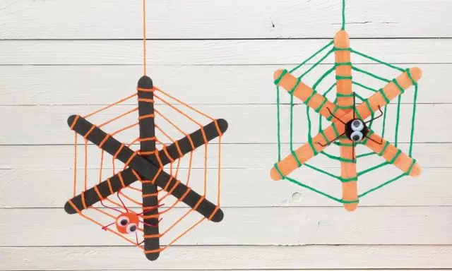 Zwei selbstgebastelte Spinnennetze aus Eisstielen und Wolle, mit kleinen Spinnen und Kulleraugen. Perfekt zum Spinnennetz basteln für Halloween!