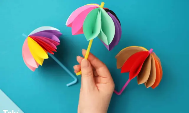 Bunte Papier-Regenschirme, tolle bastelideen einfach und schnell für Kinder. Ein gelber Schirm wird von einer Hand gehalten.