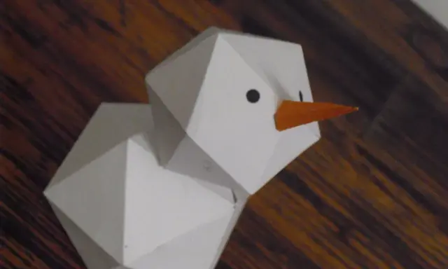 Geometrischer Schneemann, gefaltet aus Papier, mit orangefarbener Karotte als Nase und schwarzen Augen.