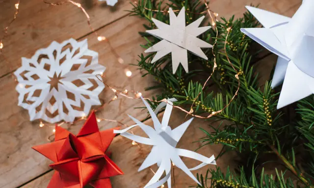 Zauberhafte Papier bastelideen Weihnachten einfach: Sterne aus Papier, Tannenzweige und Lichterkette auf Holz.
