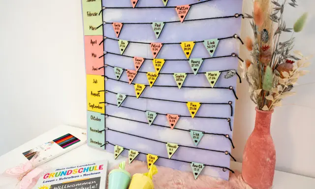 Geburtstagskalender basteln: Bunte Wimpel mit Namen und Geburtstagen hängen an Schnüren, die nach Monaten geordnet sind.
