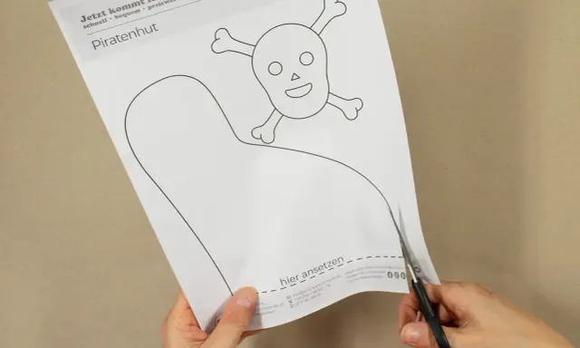 Schere schneidet Vorlage für einen Piratenhut mit Totenkopf. So einfach lässt sich ein Piratenhut basteln!