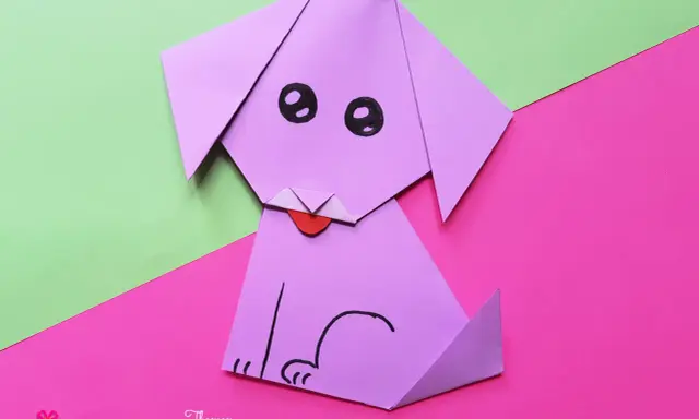 Ein lila **Falten Hund** sitzt auf pinkem und grünem Papier. Er hat schwarze Augen und eine rote Zunge.